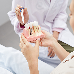 A dental professional demonstrates a mouth model with a toothpaste applicator, assisting a patient who holds a toothbrush.